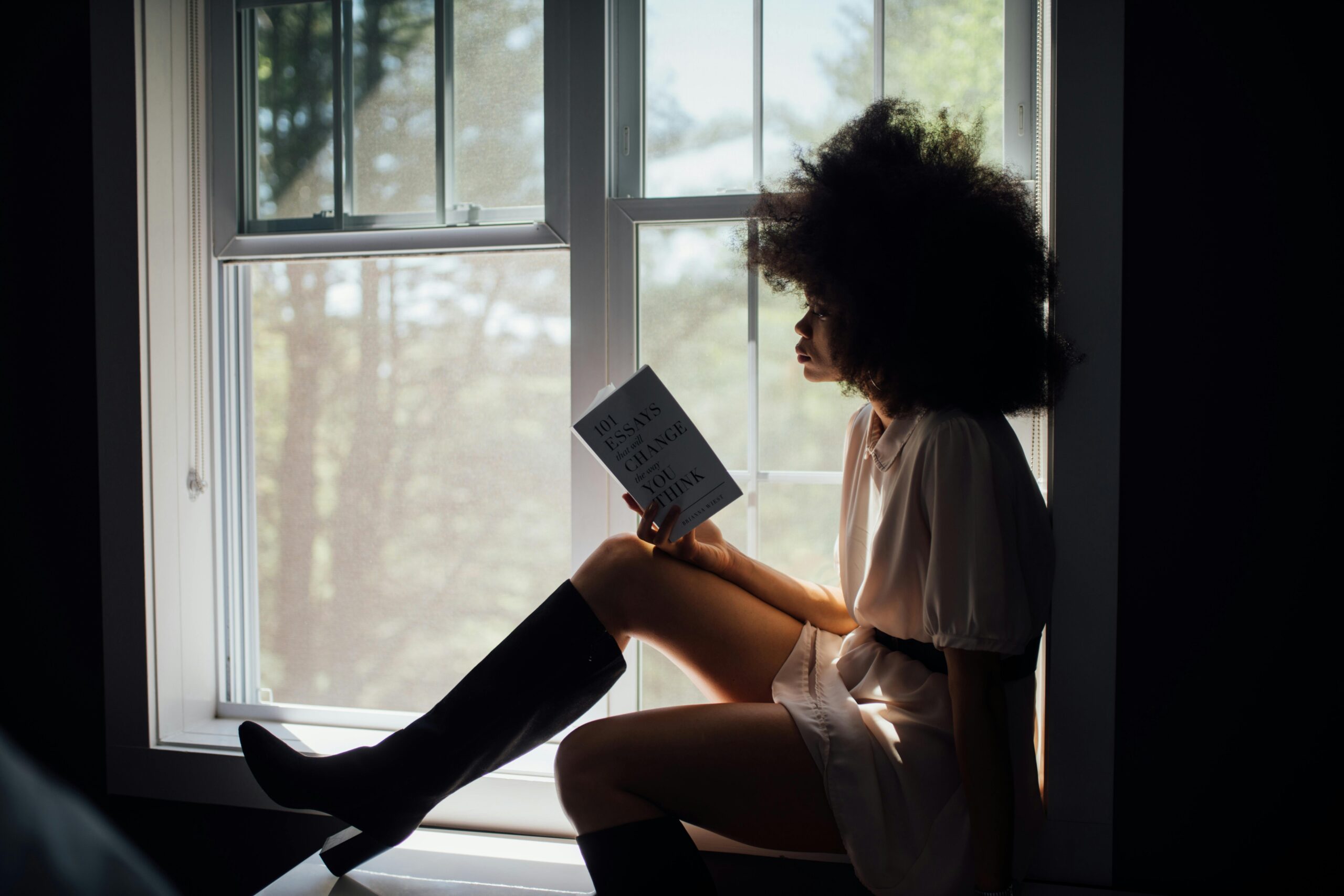 A woman enjoys a peaceful reading session by a window, bathed in natural light.